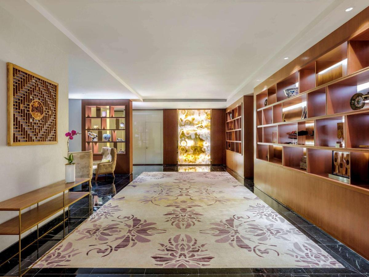 Paradox Singapore Merchant Court At Clarke Quay Екстериор снимка The photo shows a sleek and modern interior space, likely a lobby or lounge area. The floor is adorned with a large, elegant rug featuring floral patterns in soft colors. On one side, there is a wooden shelf filled with decorative items and books, al