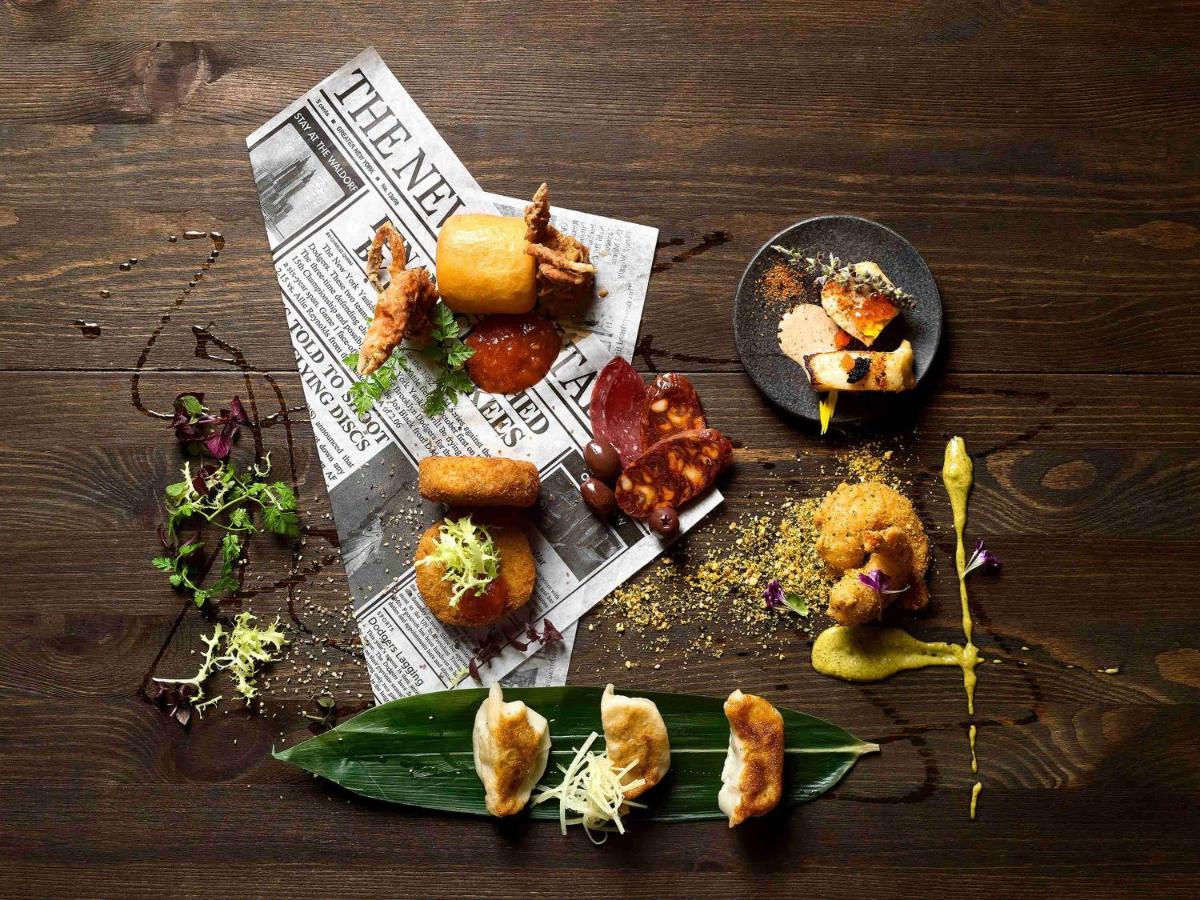 Paradox Singapore Merchant Court At Clarke Quay Екстериор снимка The photo displays an artistic arrangement of various food items on a dark wooden table. The food is positioned atop a crumpled newspaper, creating a casual yet sophisticated dining presentation. 

There are several pieces of fried food, including wh