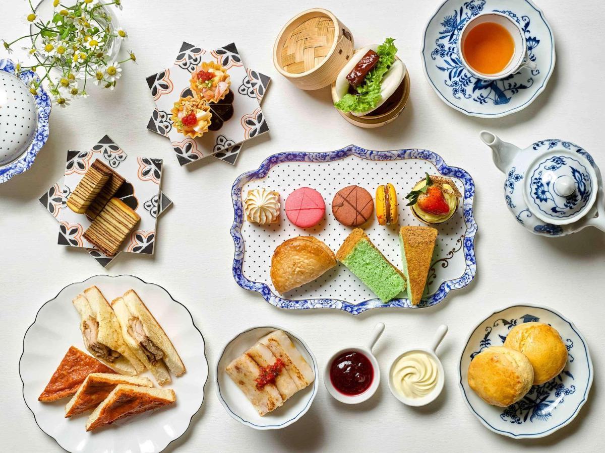 Paradox Singapore Merchant Court At Clarke Quay Екстериор снимка The photo displays a beautifully arranged assortment of food items, likely presented for an afternoon tea or dessert setting. 

- In the center, there is a decorative platter featuring a variety of pastries, including colorful macarons, small cakes, 