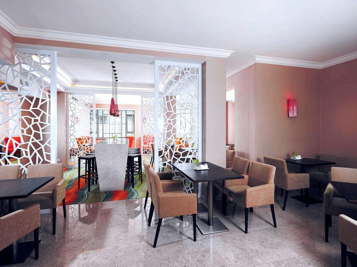 Paradox Singapore Merchant Court At Clarke Quay Екстериор снимка The photo shows a modern restaurant interior. There are several tables arranged with dark surfaces and comfortable beige chairs. The walls are painted in neutral tones, and there are decorative partition screens with an abstract pattern that adds a c