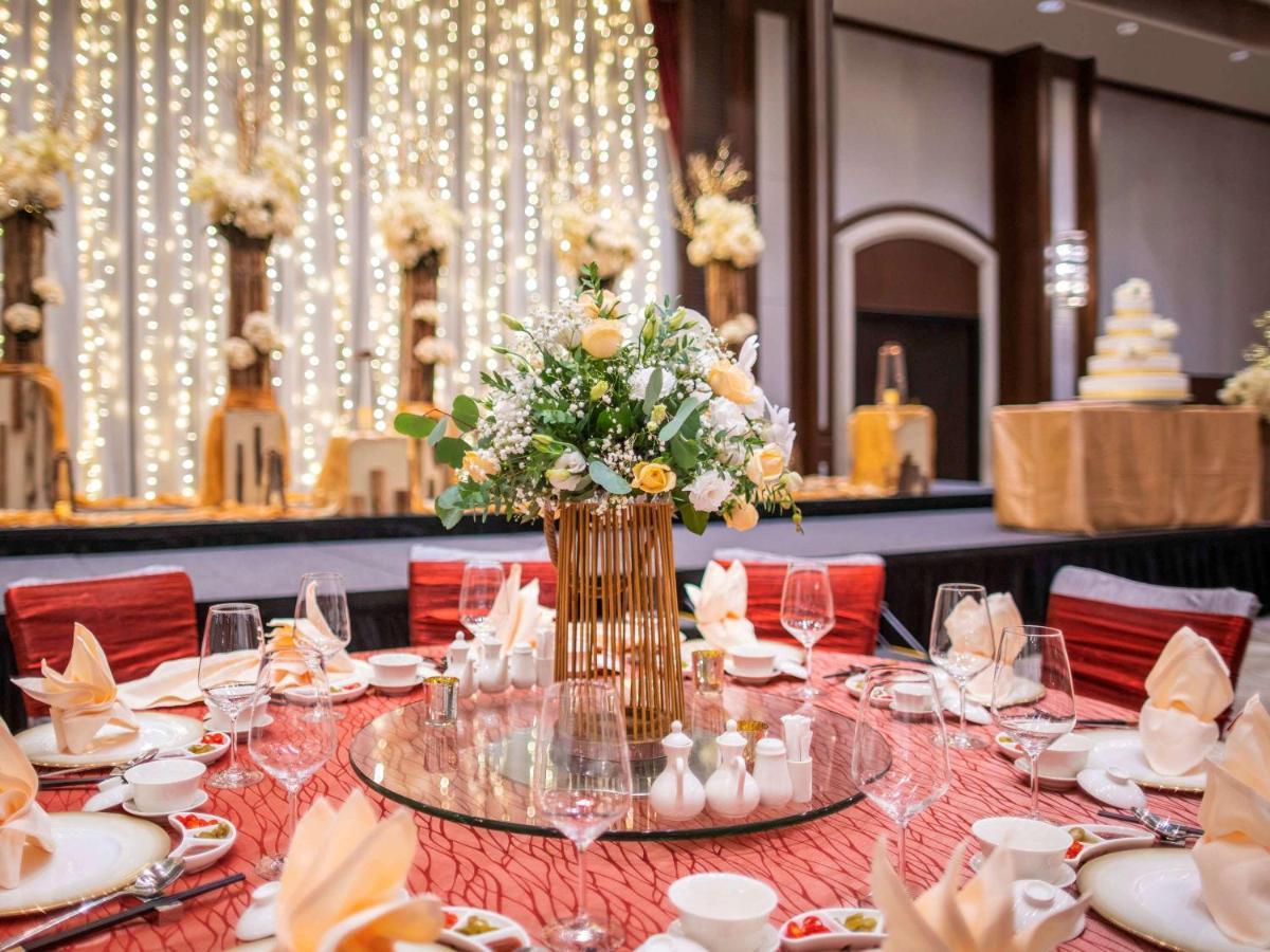 Paradox Singapore Merchant Court At Clarke Quay Екстериор снимка The photo depicts an elegantly arranged dining setup for a formal event. In the foreground, there is a round table covered with a textured red tablecloth. The table is adorned with various dining ware, including plates, cups, wine glasses, and beauti