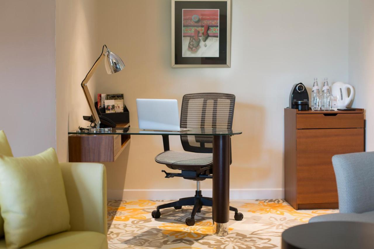 Paradox Singapore Merchant Court At Clarke Quay Екстериор снимка The photo shows a workspace setup in a well-lit room. It features a modern desk with a glass top and a comfortable office chair. On the desk, there is a laptop and a desk lamp for illumination. To the side, there are some accessories and a coffee mac