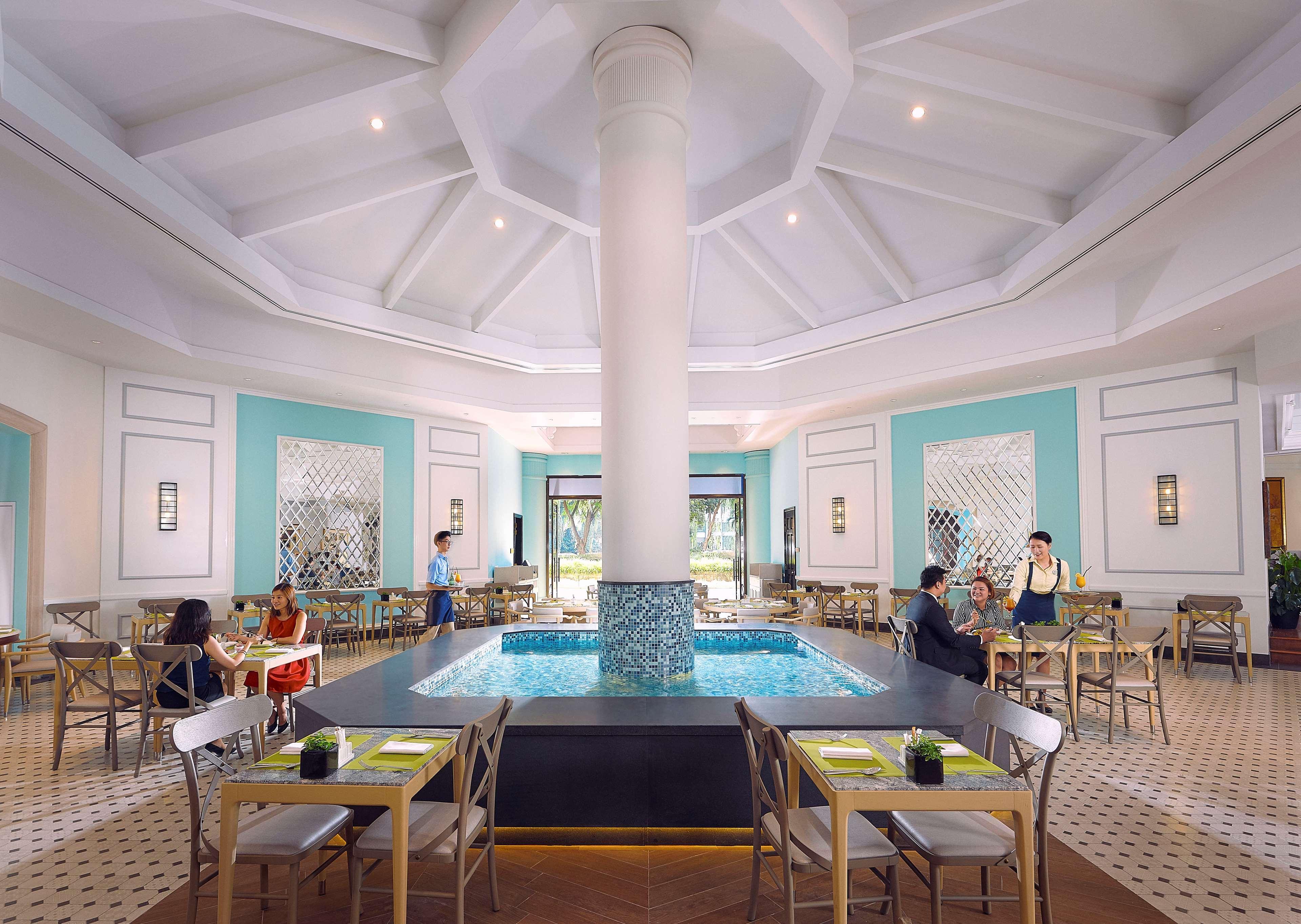 Paradox Singapore Merchant Court At Clarke Quay Екстериор снимка The photo depicts an elegant restaurant interior characterized by a spacious, well-lit design. At the center, there is a large, round column that supports a high, intricately designed ceiling. Surrounding the column is a small pool of water, adding a