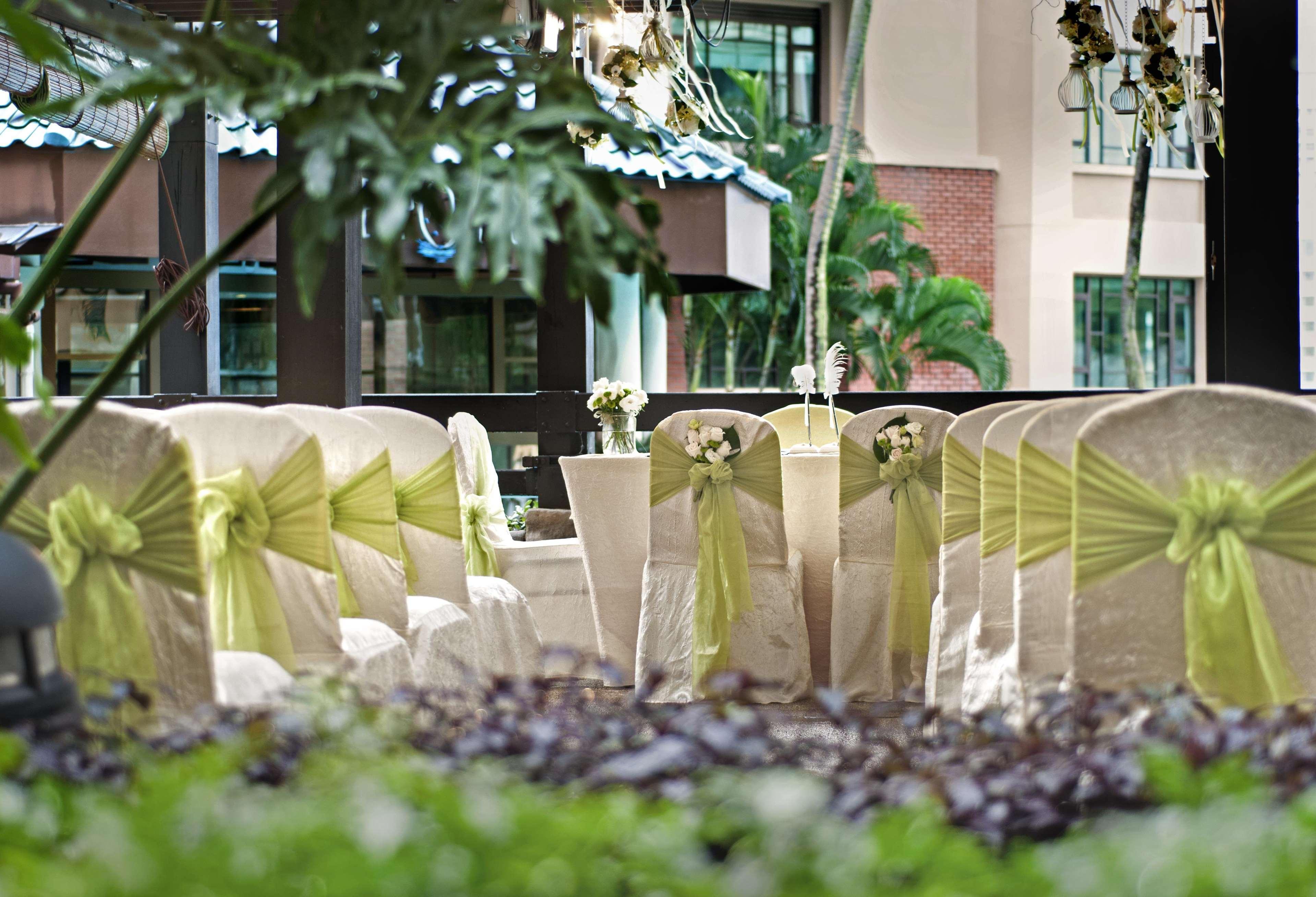 Paradox Singapore Merchant Court At Clarke Quay Екстериор снимка The photo shows a decorated setting for an event, likely a wedding or a formal gathering. There are several chairs covered in light fabric with green sashes tied around them, creating an elegant look. In the foreground, there are potted plants and gr