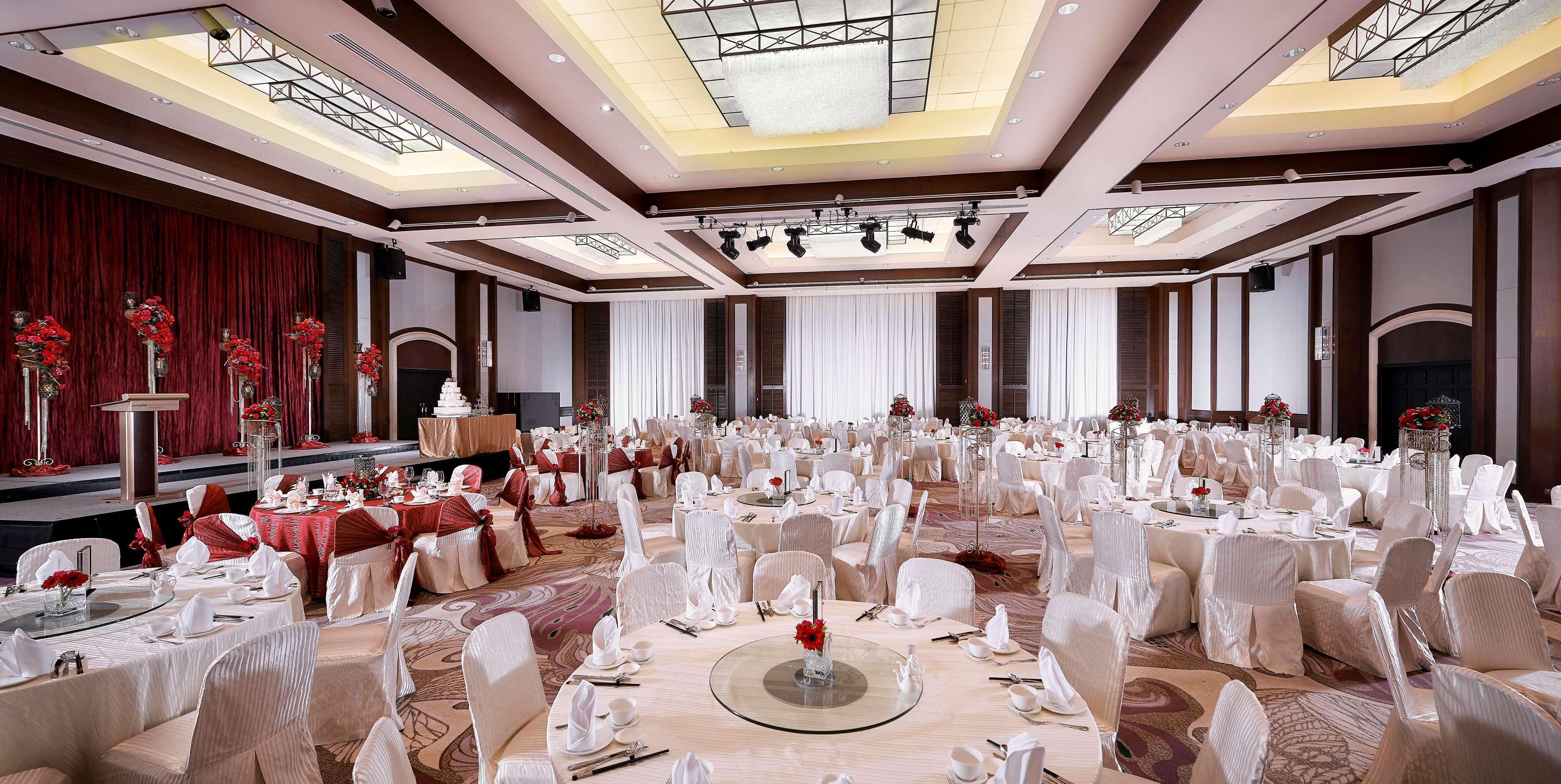 Paradox Singapore Merchant Court At Clarke Quay Екстериор снимка The photo shows a spacious banquet hall set up for an elegant event. Round tables are beautifully arranged, each covered with a tablecloth and adorned with a center decoration featuring red flowers. The chairs are draped in white covers, adding to th
