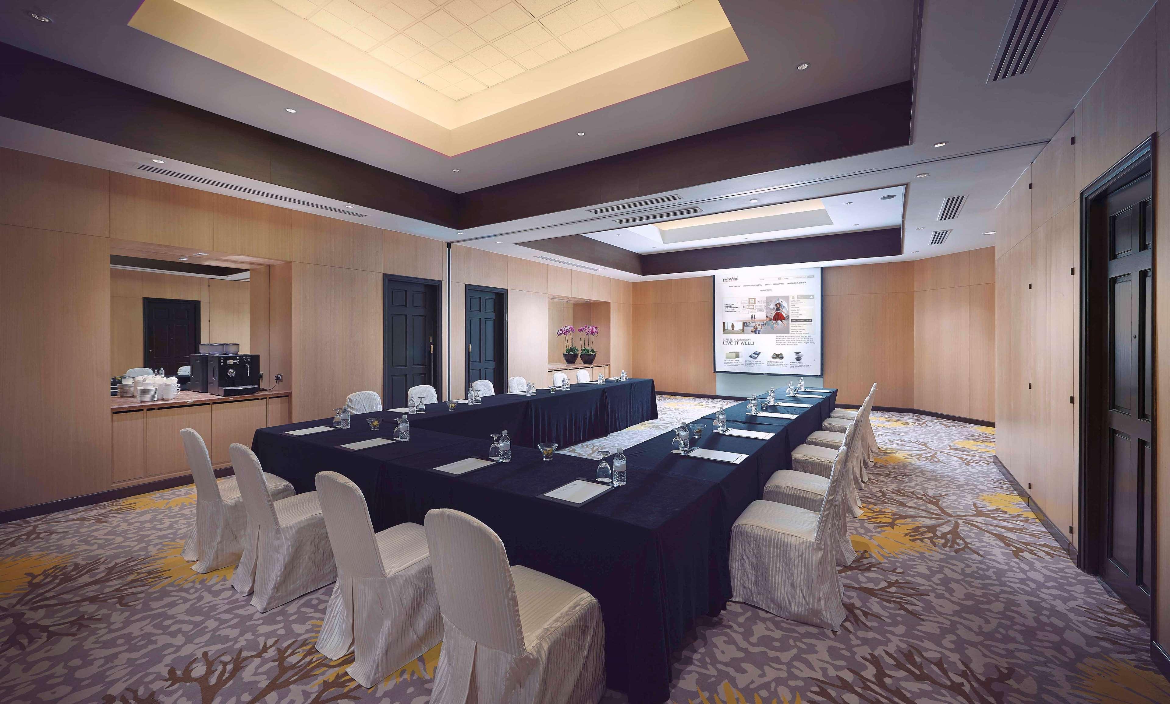Paradox Singapore Merchant Court At Clarke Quay Екстериор снимка The photo shows a conference room designed for meetings or presentations. It features a long rectangular table covered with a black tablecloth, surrounded by white chairs. There are glass water pitchers and glasses on the table. The room has wooden p