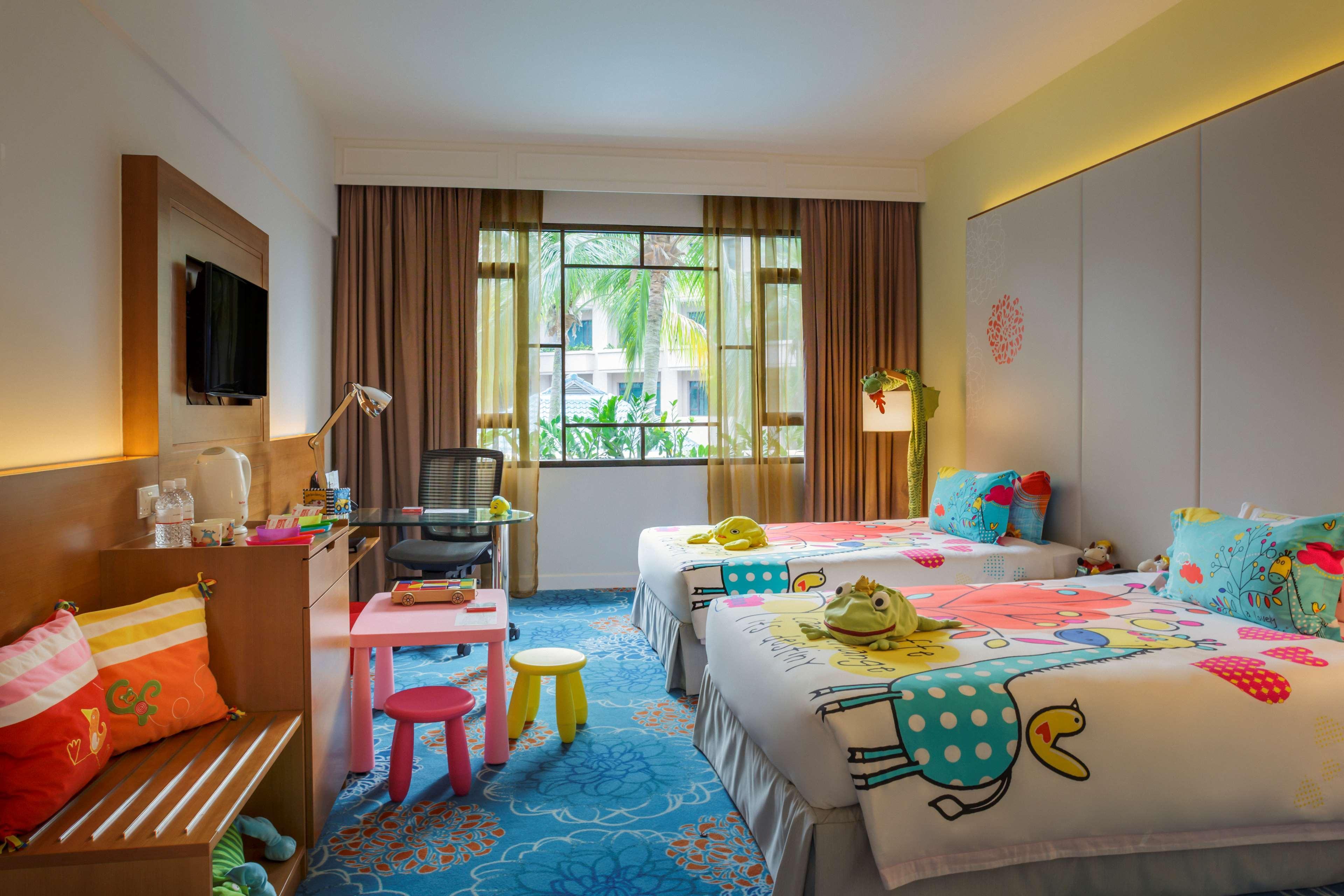Paradox Singapore Merchant Court At Clarke Quay Екстериор снимка The photo shows a brightly colored hotel room designed in a family-friendly style. There are two twin beds, each adorned with playful, colorful bedding featuring whimsical patterns. A small table with brightly colored stools is positioned nearby. A c