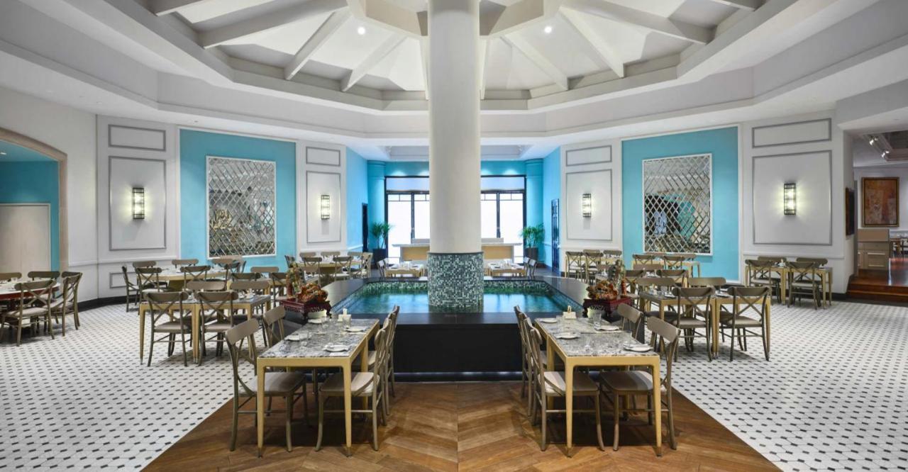 Paradox Singapore Merchant Court At Clarke Quay Екстериор снимка The photo depicts an elegantly designed restaurant interior. The space features a high, domed ceiling with a central pillar. The walls are painted in a vibrant blue, complemented by decorative mirrors and artwork. There are several tables arranged th